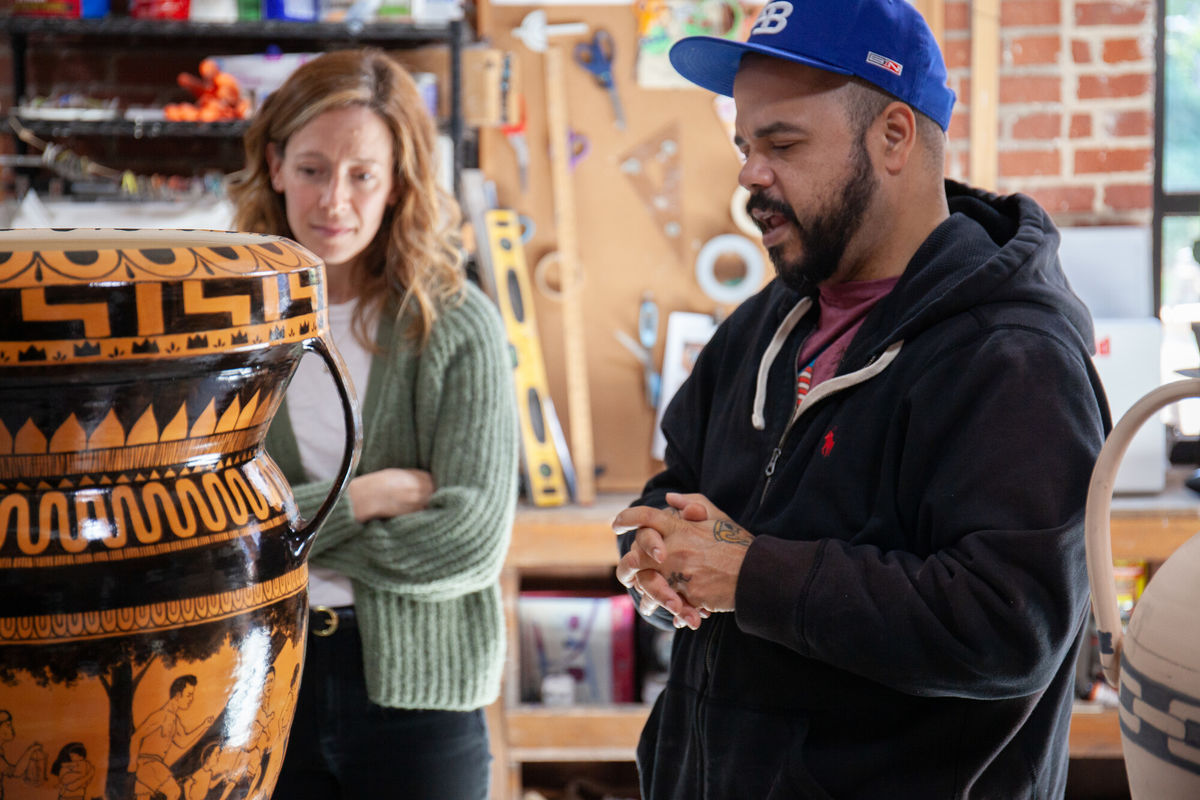 A man and a woman look closely at a large black and orange painted ceramic