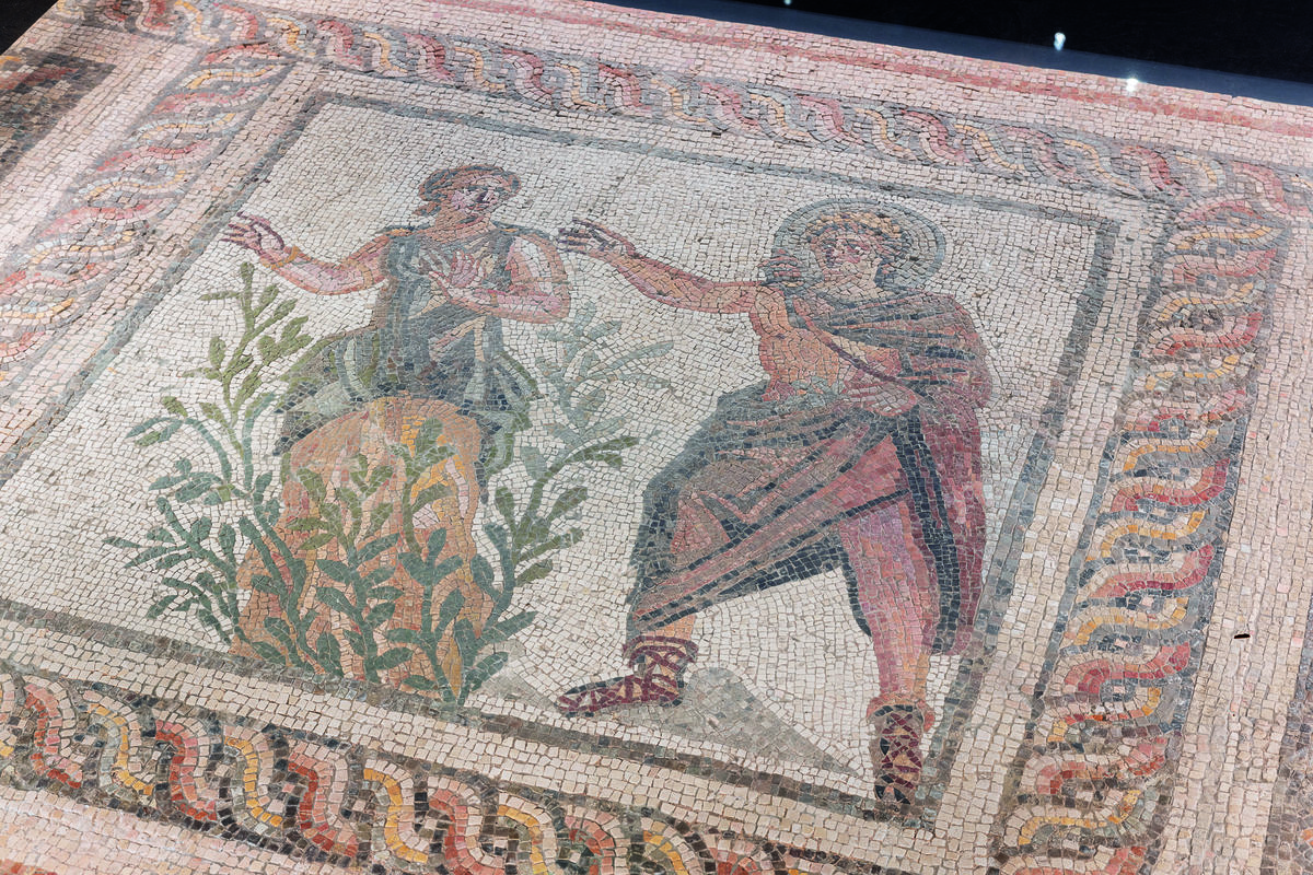 detail of an ancient mosaic with a man reaching his arm out at a female who looks to be trying to get away