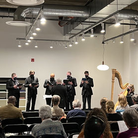A group of people wearing dark clothing sing in front of an audience in front of a white wall