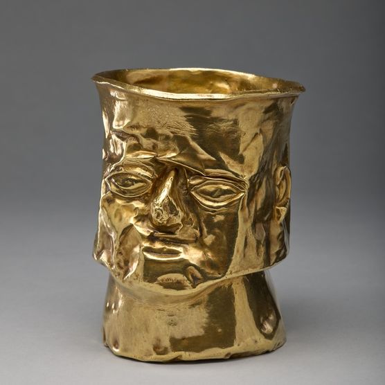 A gold cup shaped in the likeness of a man's face, with a square jaw and serious expression