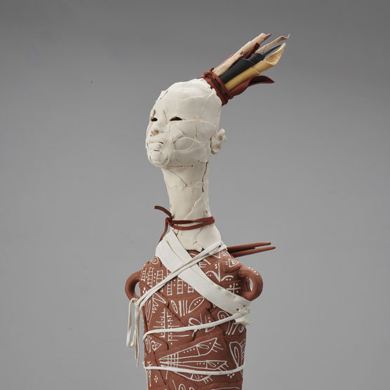 A ceramic figure with a white head wearing a crown. The body has two small loops for arms