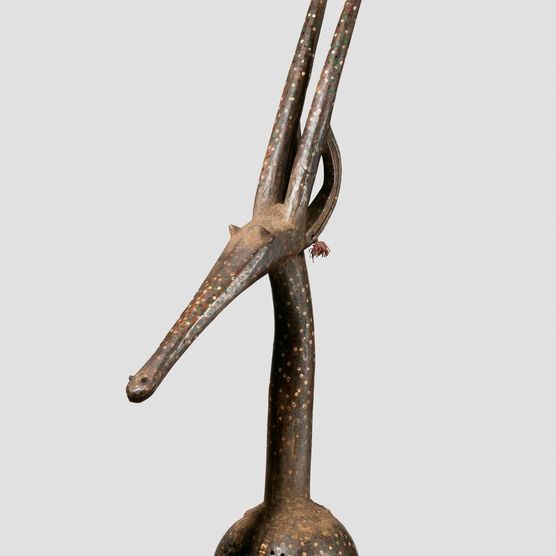 A graceful elongated wood-carved antelope, medium brown, dotted with green, red, and yellow