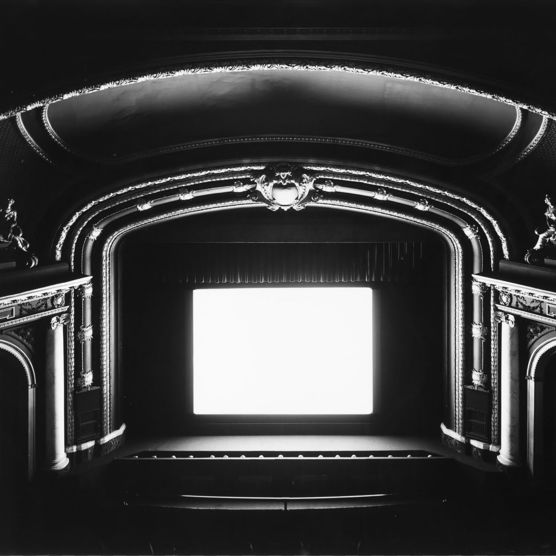 Black and white image of a theatre with a white rectangle screen on the stage.