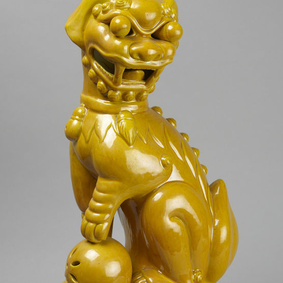 Bright yellow sculpture of seated lion, with dog-like ears, round eyes, with one paw on a ball