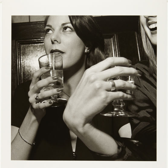 A sepia toned photograph of people holding drinks in glasses, shot from below