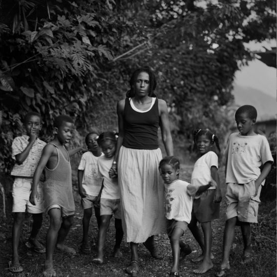 A b-and-w image of a Black woman surrounded by a group of young Black children in lush outdoor scene