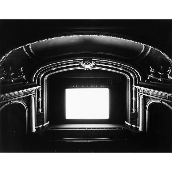 Black and white interior view of a theater with a screen glowing bright white.