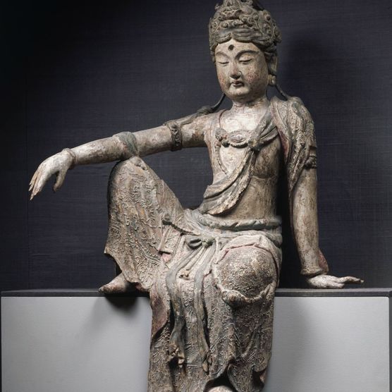 Statue of a figure wearing a loosely draped robe, bracelets, and an ornate crown