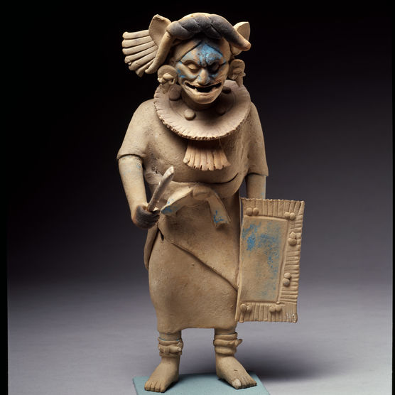 A light tan sculpture of a warrior, teeth bared, jaguar ears flared. Traces of cerulean pigment.