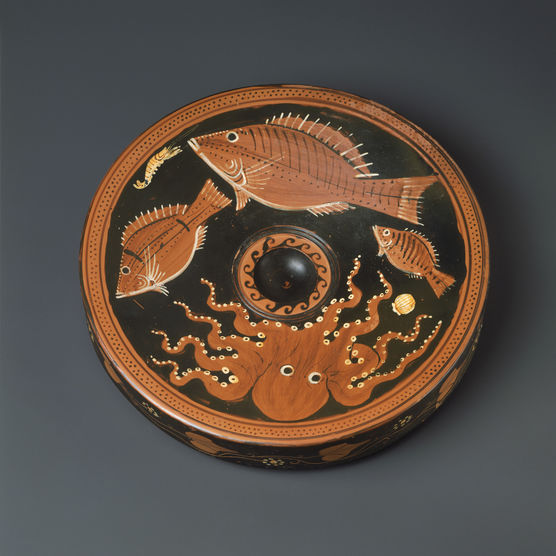 A black plate decorated with three red fish of different sizes and an octopus