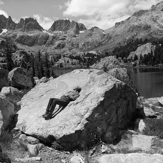 Black and white image of a person lying on their back on a large rock in nature