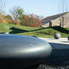 An ovoid stone sculpture in the foreground with round smaller ball shapes in an outdoor setting.