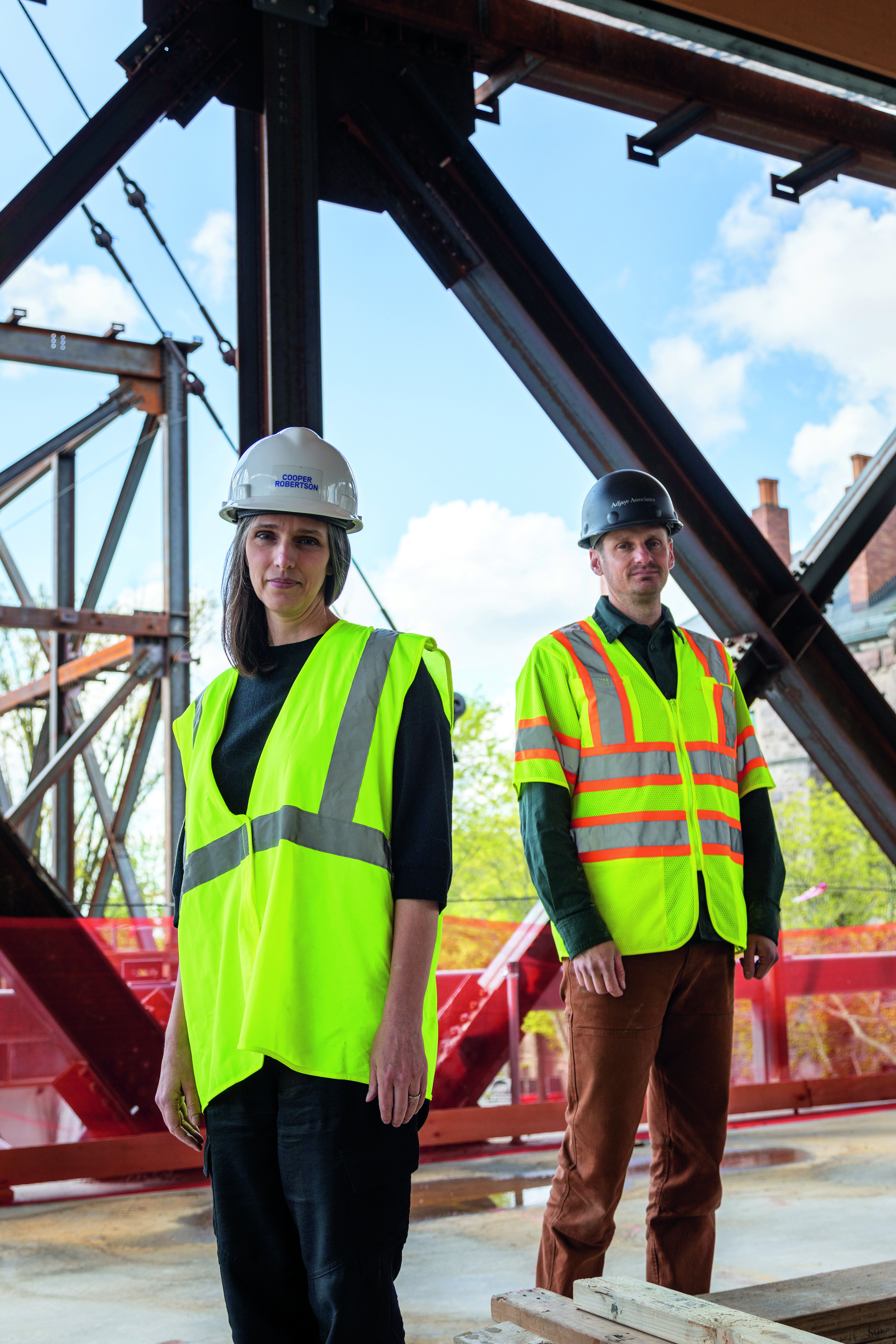 Portrait of two people on a construction site wearing hardhats and safety vests.