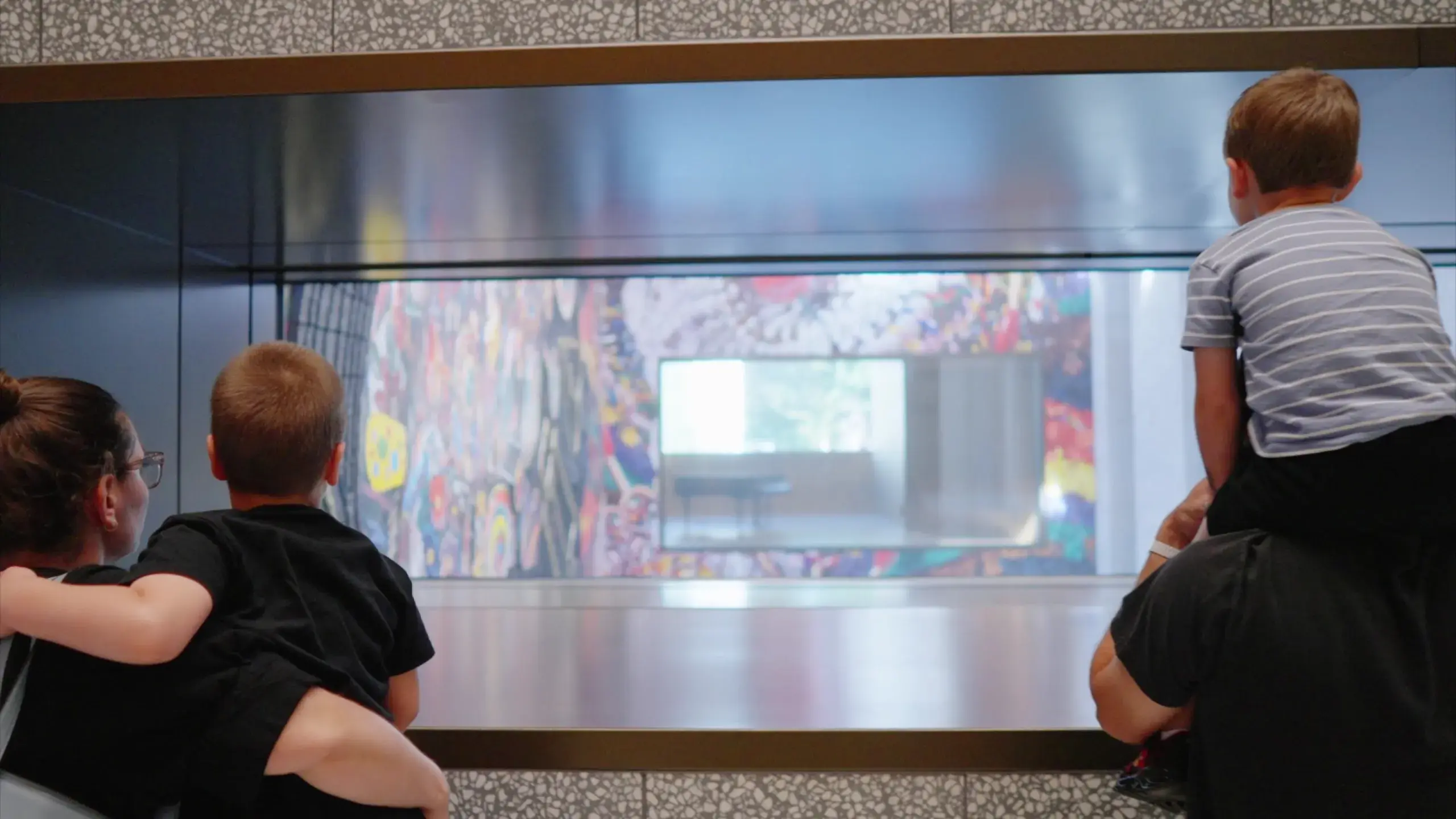 A family stares through a window looking at Nick Cave's colorful mosaic, "Let me kindly introduce myself. They call me MC Prince Brighton". 