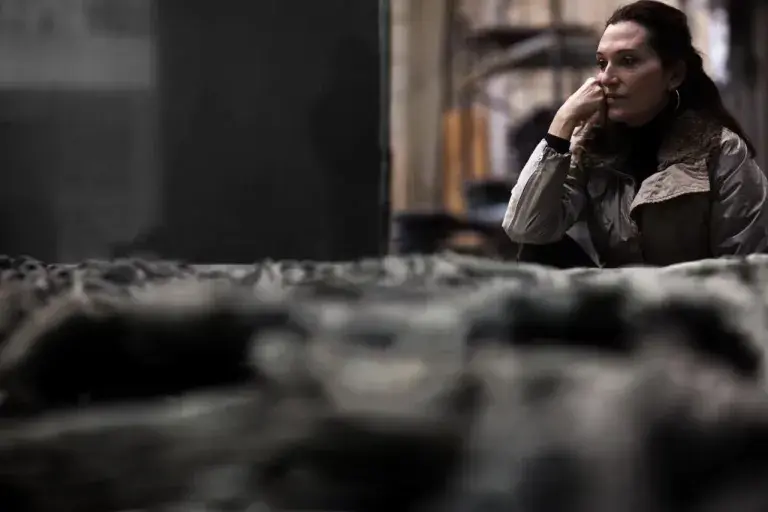 A woman sits pensively behind a sculpture.