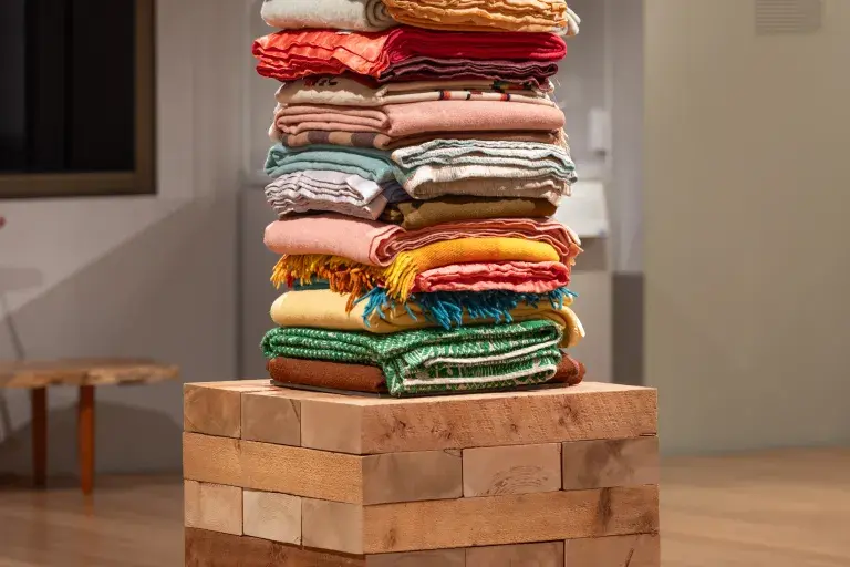 A stack of colorful folded quilts and blankets on a square wooden plinth.