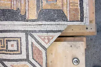 Detail of a mosaic with black, white, and red tesserae in a geometric pattern on a section of plywood.