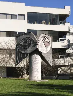 A concrete sculpture of an abstract face set outside in front of a building