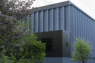 Gray building with green plants and trees in front.