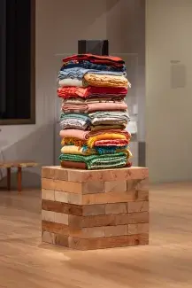 A stack of colorful folded quilts and blankets on a square wooden plinth.