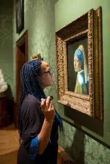 A woman stands close and inspects a painting of a woman with a headscarf and pearl earring