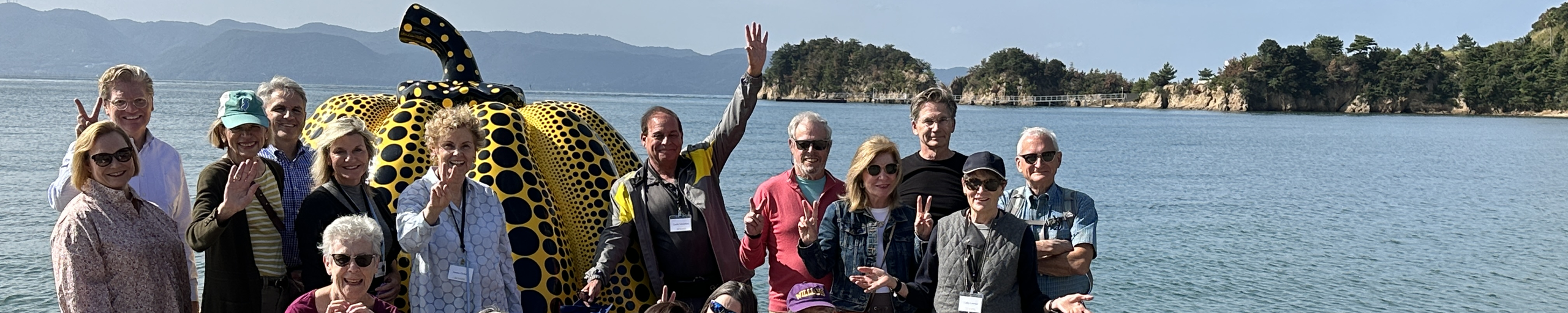 Group of smiling people standing in front of a pumpkin sculpture on the side of a lake.